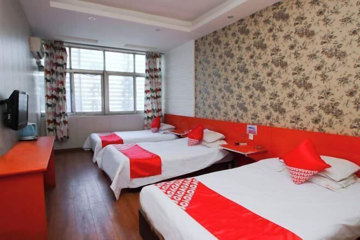 A hotel room with two beds, a TV, a desk, and a window with curtains.