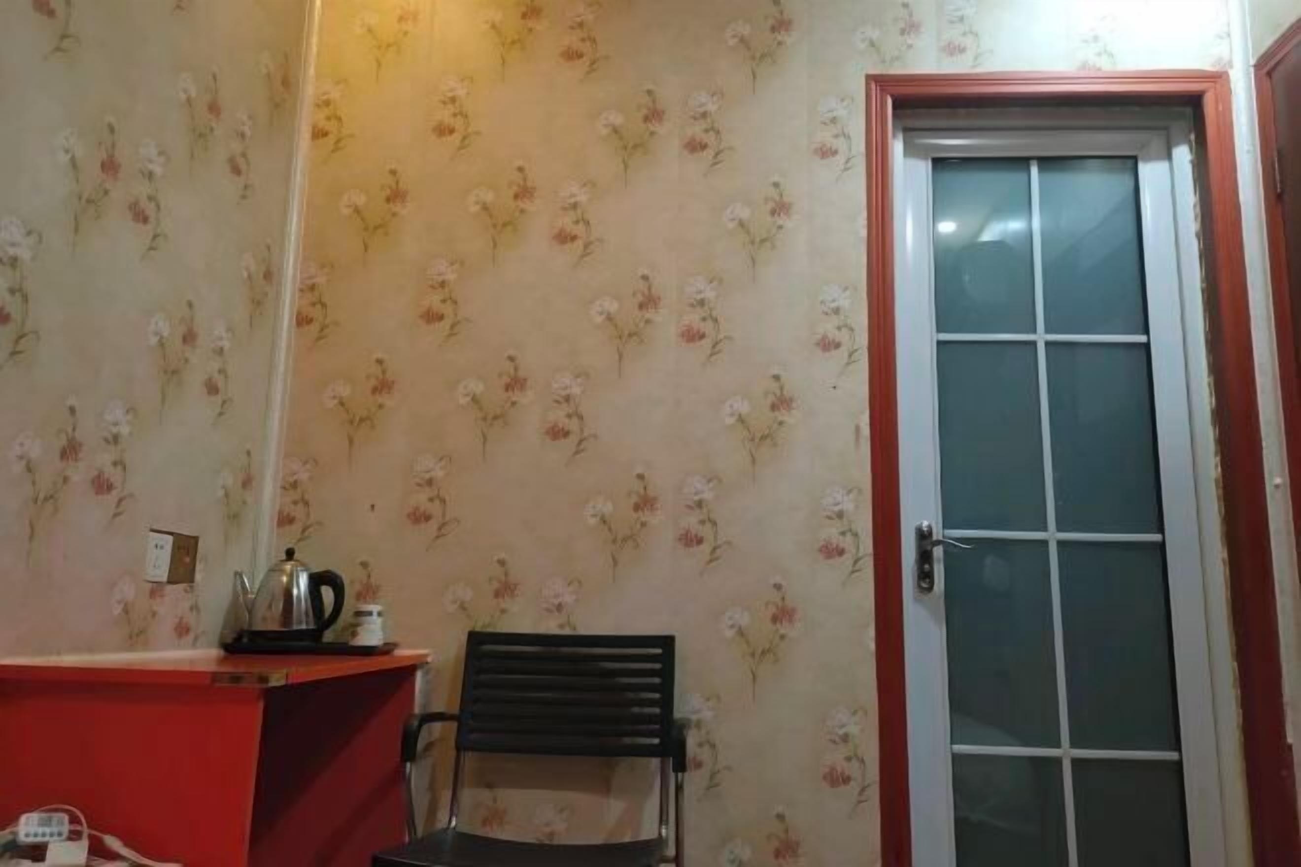 Um quarto com papel de parede floral, um balcão vermelho, uma cadeira preta e uma porta de vidro.