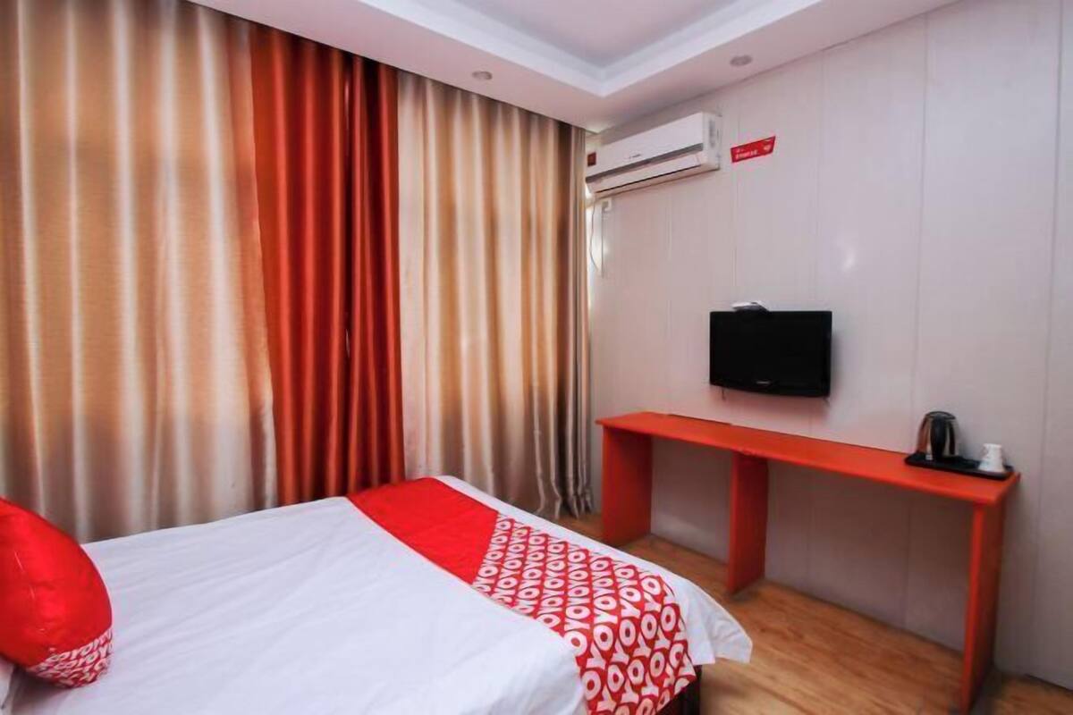 A hotel room with a bed, a TV, a desk, and an air conditioning unit.