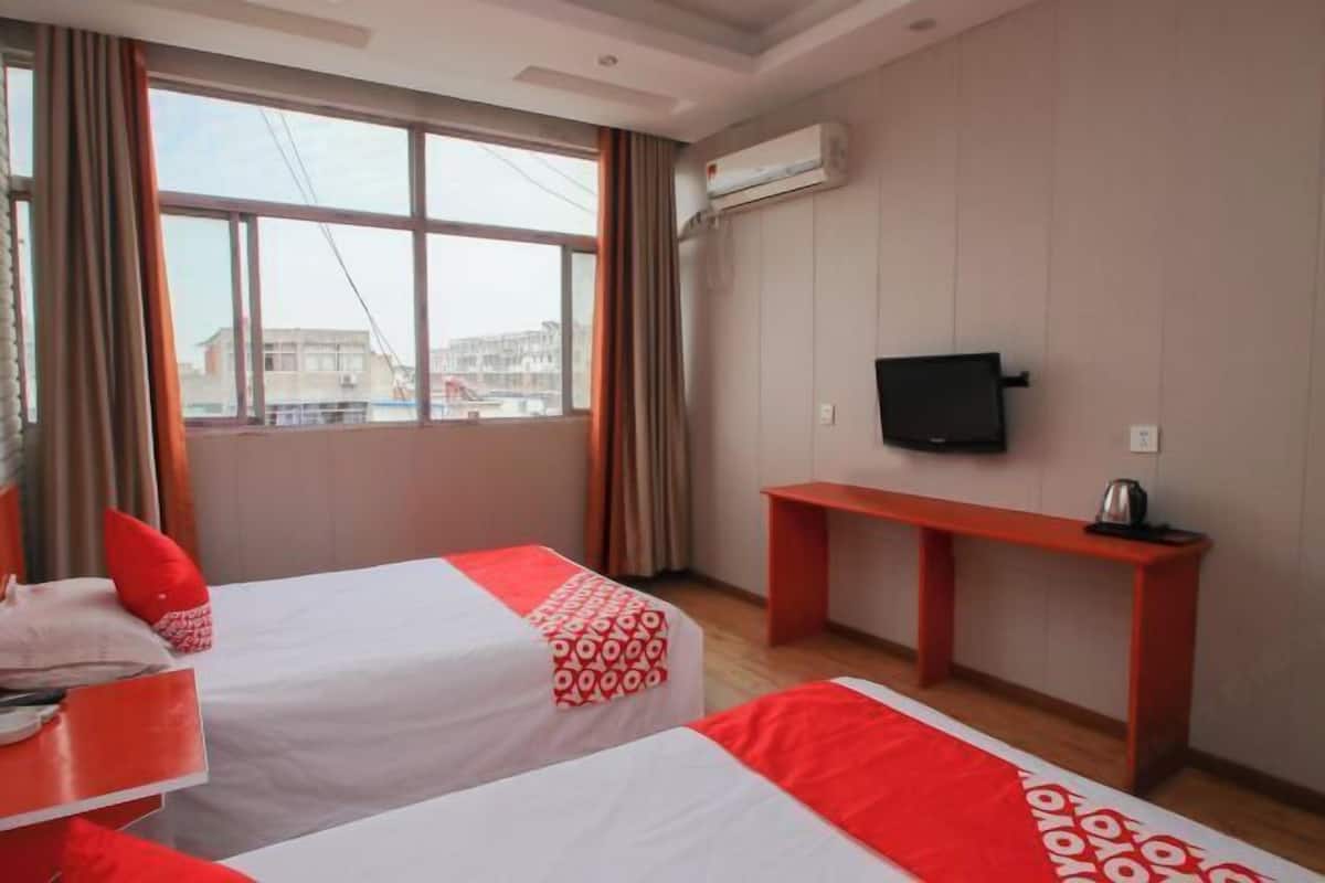 A hotel room with two beds, a TV, a desk, and an air conditioning unit.