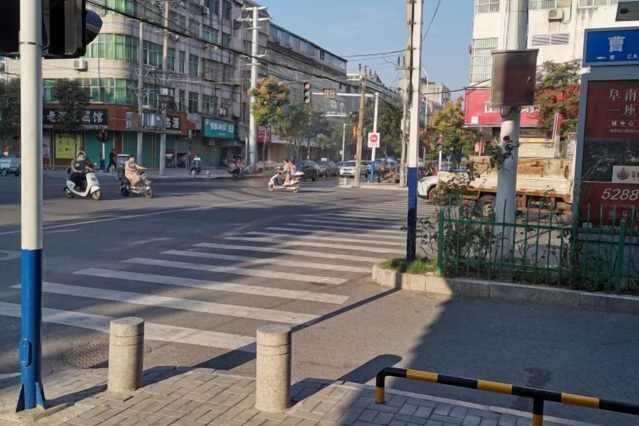 Een straatkruising met verkeerslichten, paaltjes en een zebrapad.