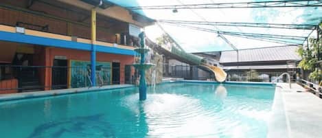 Una piscina interior con tobogán, zona techada y edificio de varios pisos.