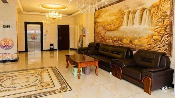 A spacious lobby with a large sofa set, a chandelier, and a mural of a waterfall.