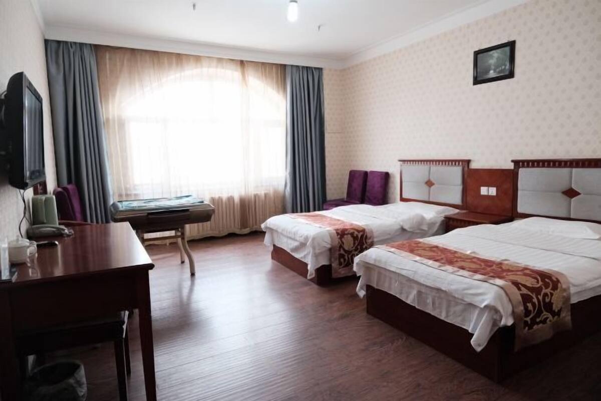 Habitación de hotel con dos camas, un escritorio, una silla y un televisor.