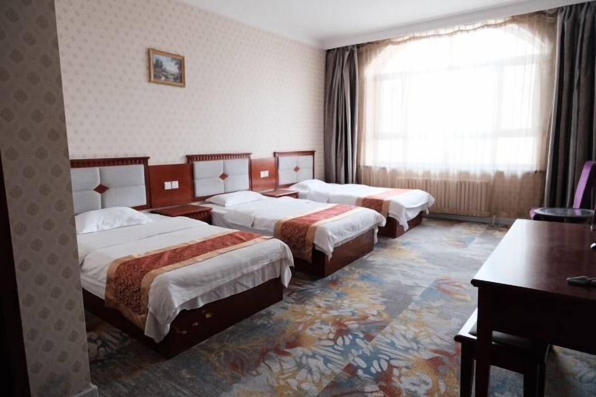 Habitación de hotel con tres camas, un escritorio de madera y un ventanal con cortinas.