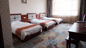 A hotel room with three beds, a wooden desk, and a large window with curtains.