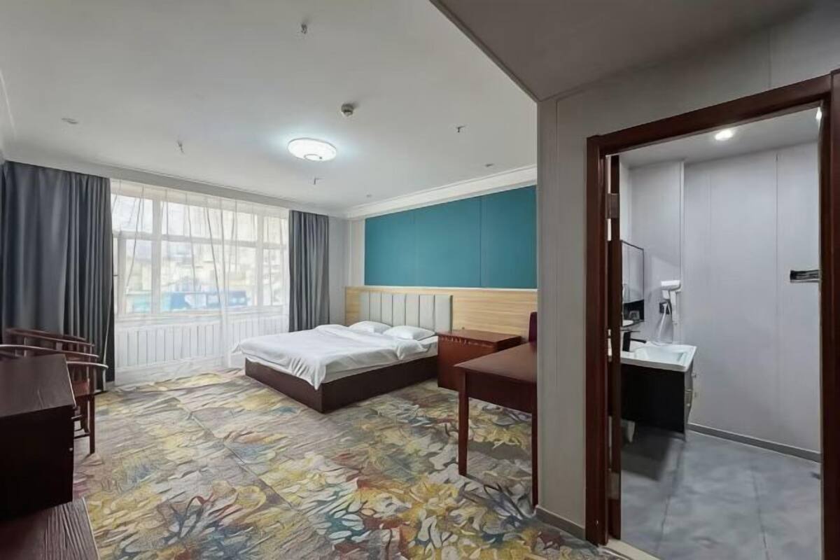 Habitación de hotel con cama, escritorio, silla, baño y un ventanal grande.