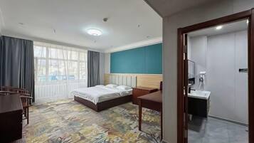 A hotel room with a bed, a desk, a chair, a bathroom, and a large window.