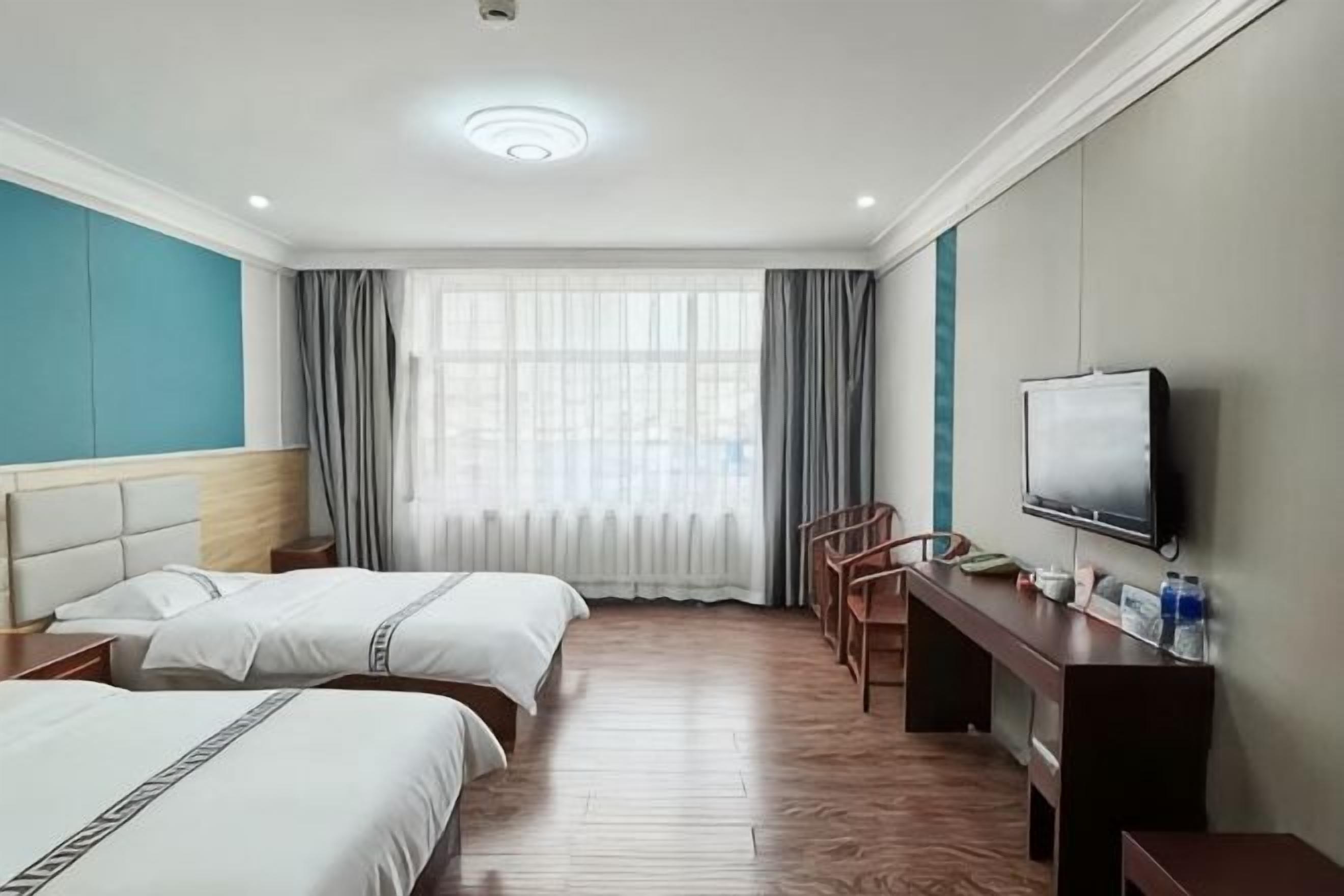 Habitación de hotel con dos camas, un escritorio, una silla, un televisor y un amplio ventanal con cortinas.
