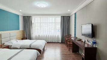 Habitación de hotel con dos camas, un escritorio, una silla, un televisor y un amplio ventanal con cortinas.