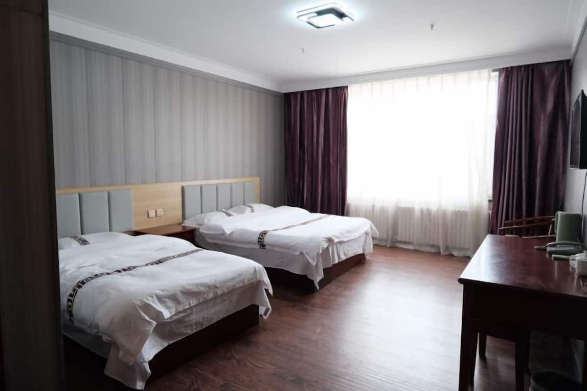 Habitación de hotel con dos camas, un escritorio de madera y una televisión.