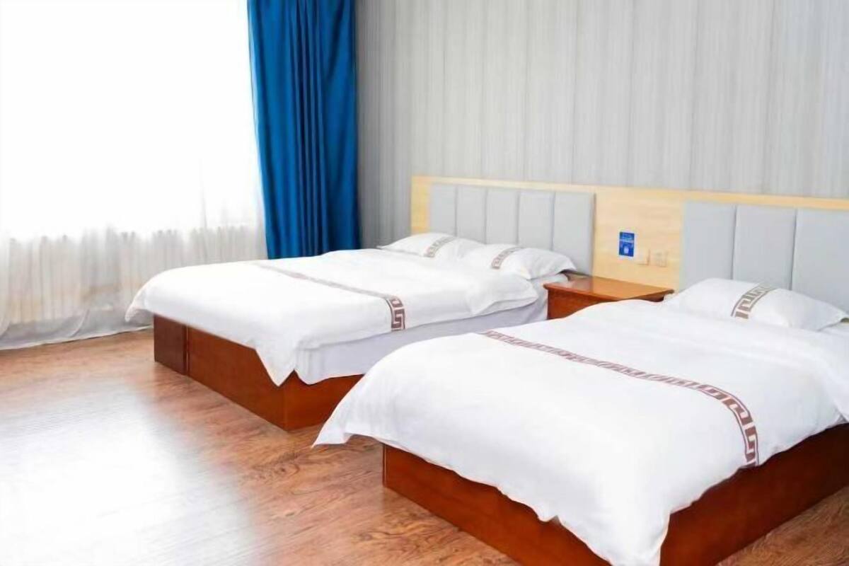 Dos camas individuales con cabeceros de madera y ropa de cama blanca, suelo de madera y una ventana con cortinas azules.