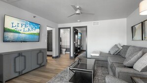 Ein modernes Wohnzimmer mit einem grauen Sofa, einem Glastisch und einem Gemälde eines Sees.