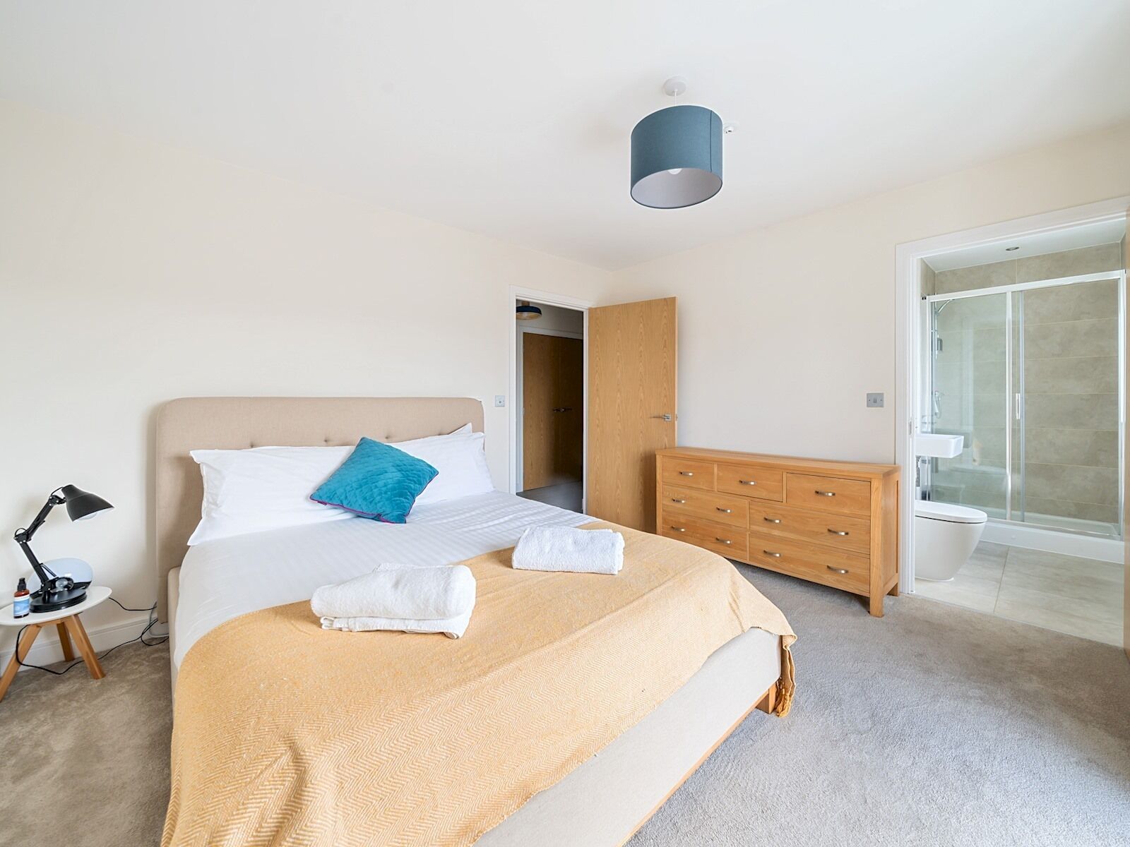 A modern bedroom with a bed, bedside lamp, and a wooden dresser.