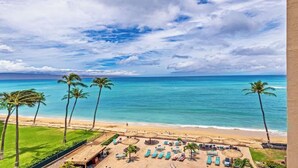 A beach view with palm trees, lounge chairs, and a clear sky.