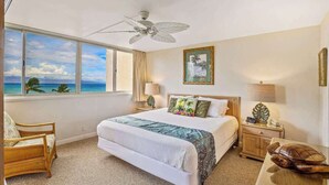 A hotel room with a bed, a chair, a nightstand, a lamp, a turtle decoration, and a view of the ocean.