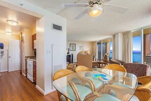 A spacious living area with a glass dining table, wicker chairs, and a ceiling fan. - Large Corner Oceanfront 2 bedroom condo, AC, wrap around lanai, walkable area (Lahaina)