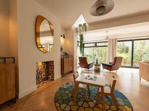 Un salon moderne avec une cheminée, une table ronde et une grande fenêtre donnant sur un paysage verdoyant.