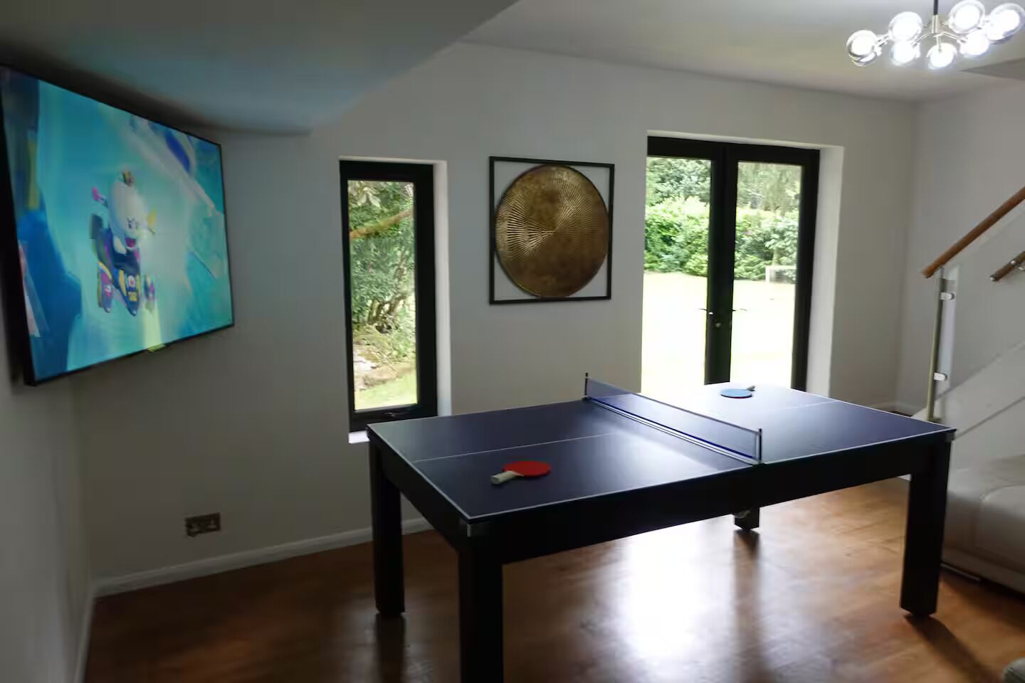 Una habitación con mesa de ping pong, televisión y ventana con vistas a la vegetación.