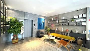 A modern interior with a sofa, a coffee table, a potted plant, and a wall-mounted shelf with various items.