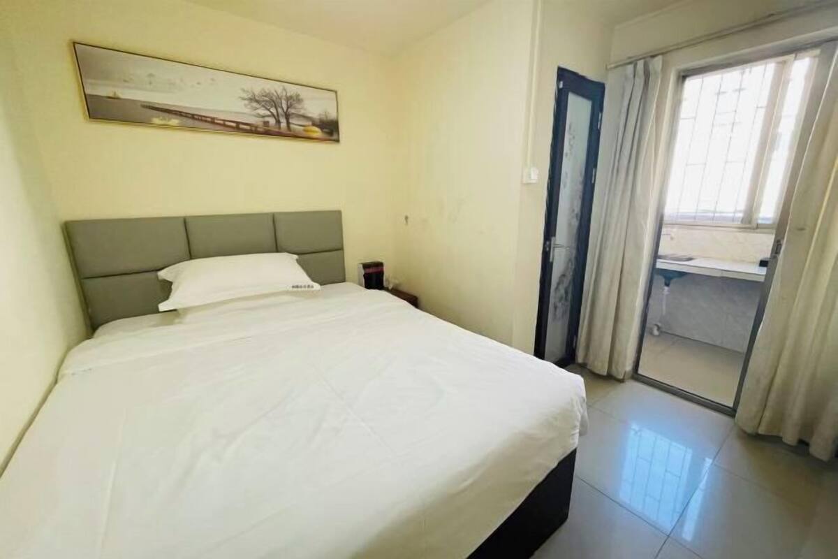 Habitación de hotel con cama, un cuadro en la pared, ventana con cortinas y puerta que da a un espacio exterior.