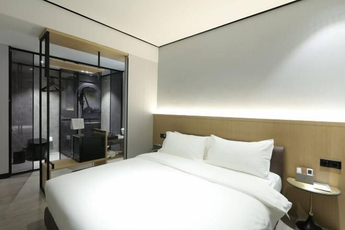 Una habitación de hotel moderna con una cama grande, una mesita de noche y un vestidor con espejo y televisor.