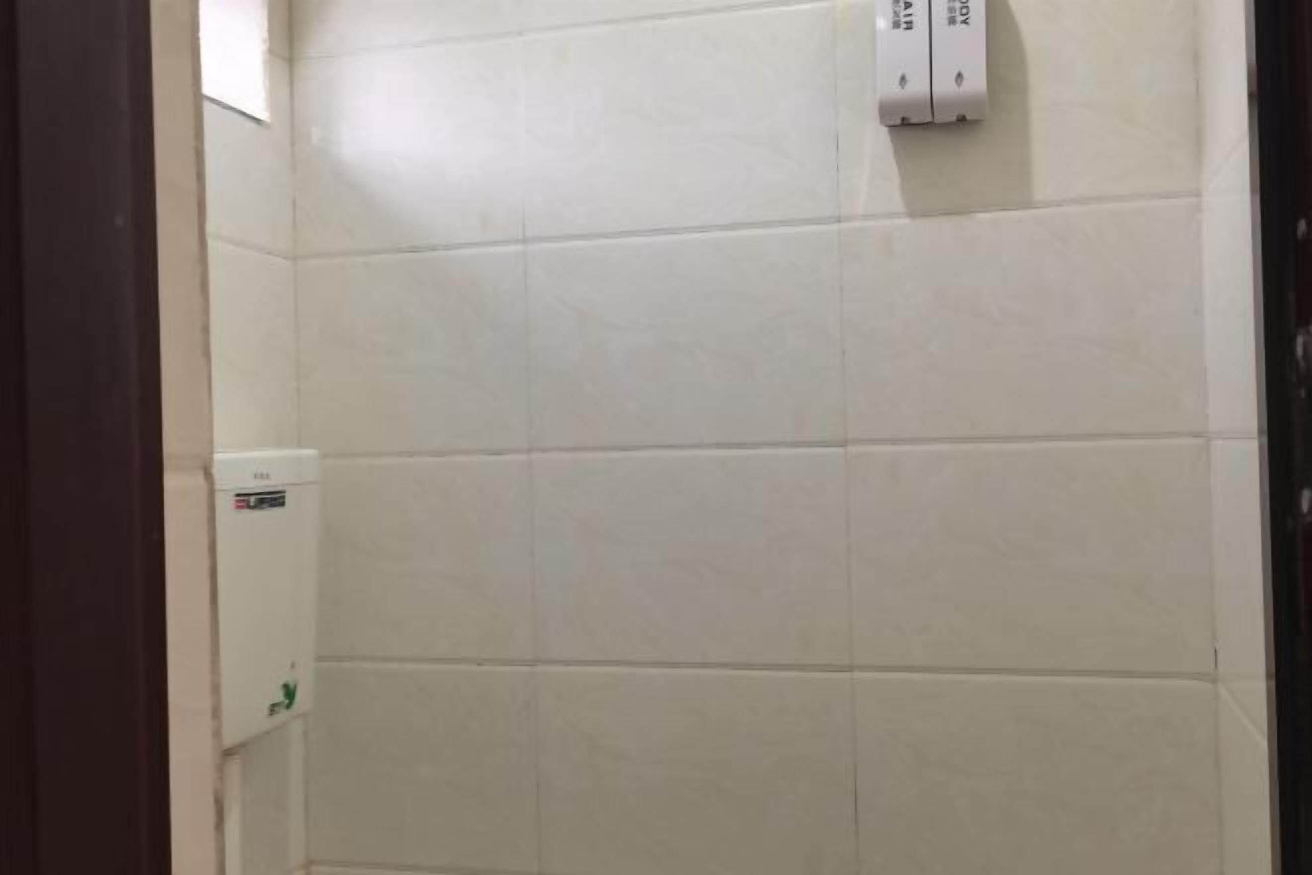 A bathroom with white tiles, a hand dryer, and a soap dispenser.
