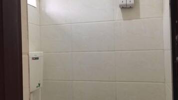 A bathroom with white tiles, a hand dryer, and a soap dispenser.