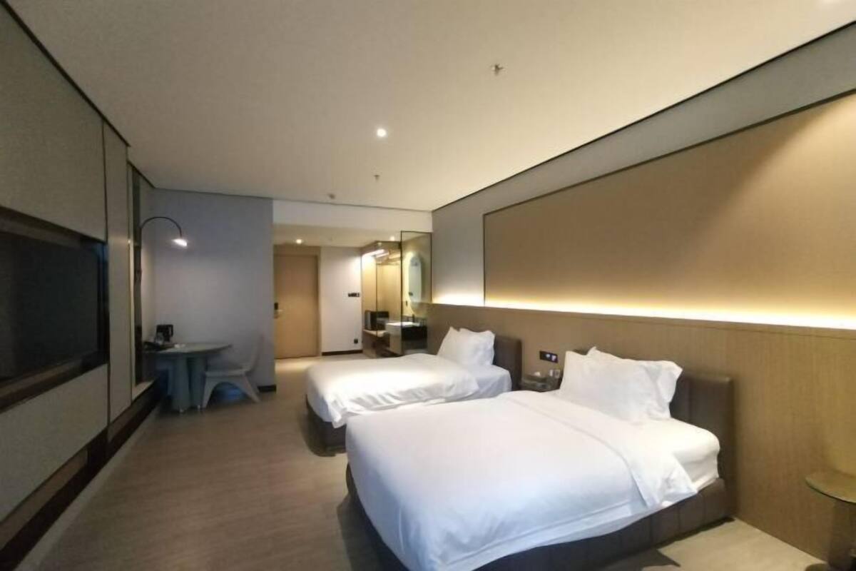 Una habitación de hotel con dos camas, una mesita, un televisor y un espejo.