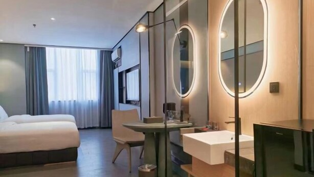 Hotellihuone, jossa on sänky, työpöytä, pyöreä peili, pesuallas ja televisio.
