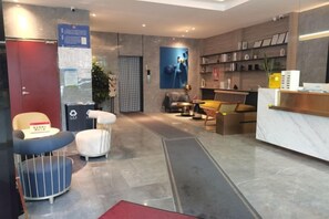 A modern hotel lobby with a reception desk, seating area, and a visible trash bin. - Ali Ecology Hotel (Shenzhen)