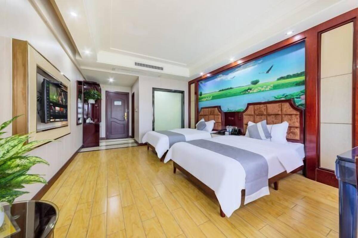 Una habitación de hotel con dos camas, un cuadro grande en la pared y suelo de madera.