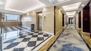 Un pasillo de hotel con piso de cuadros, pared de mármol y alfombra estampada.