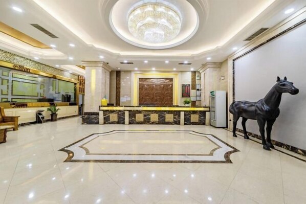 Een hotel lobby met een receptiebalie, een grote kroonluchter, een beeld van een paard en een marmeren vloer.