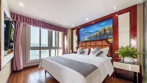 Una habitación de hotel con una cama grande, un cuadro en la pared, una ventana con cortinas y una planta sobre una mesita.