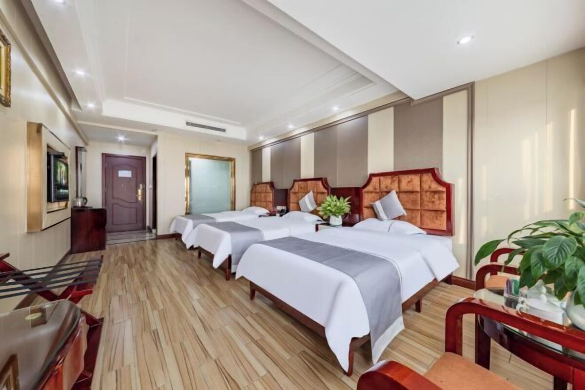 A hotel room with two beds, a desk, a chair, and a potted plant.