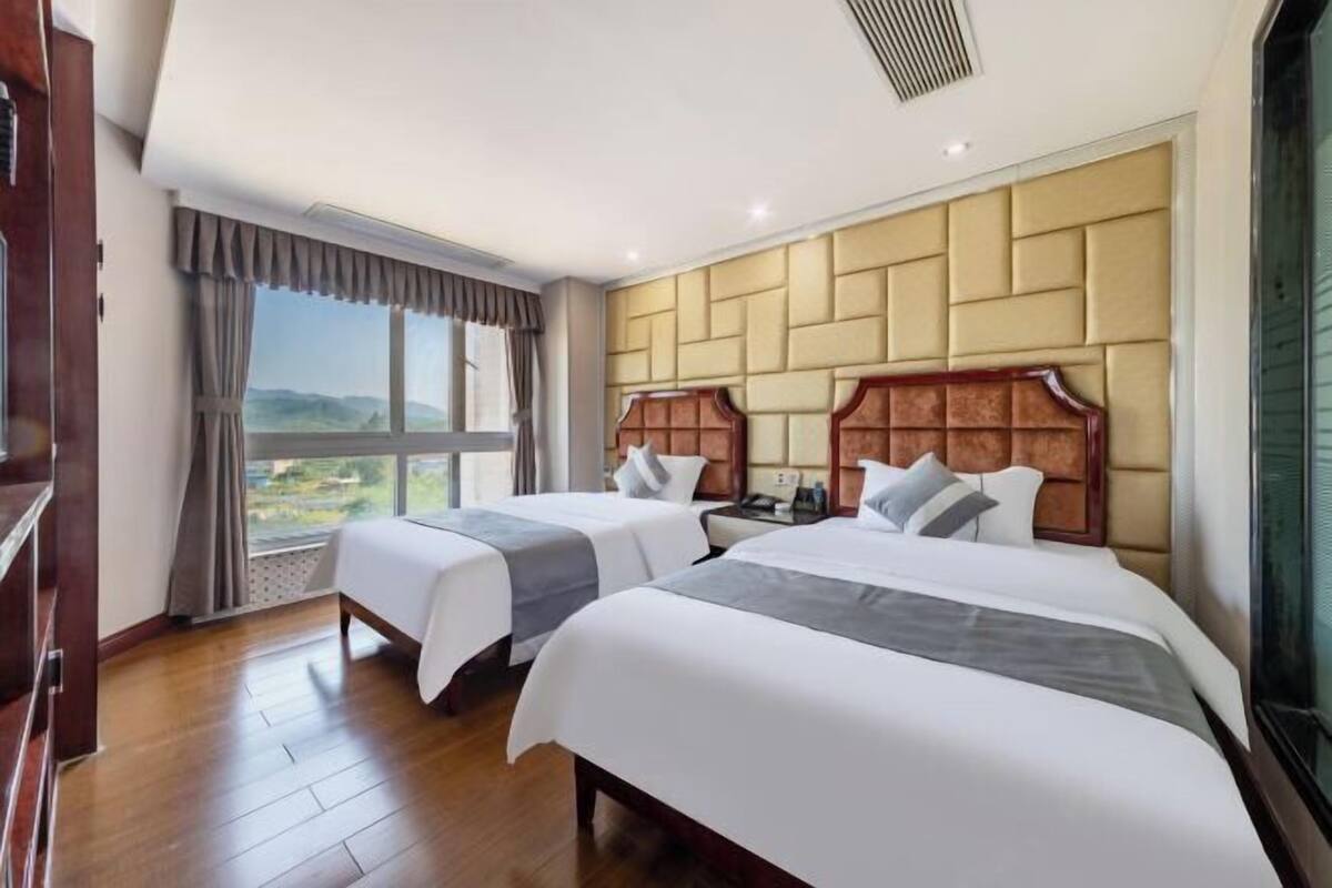 Habitación de hotel con dos camas, un ventanal con vistas y cabecero de madera.
