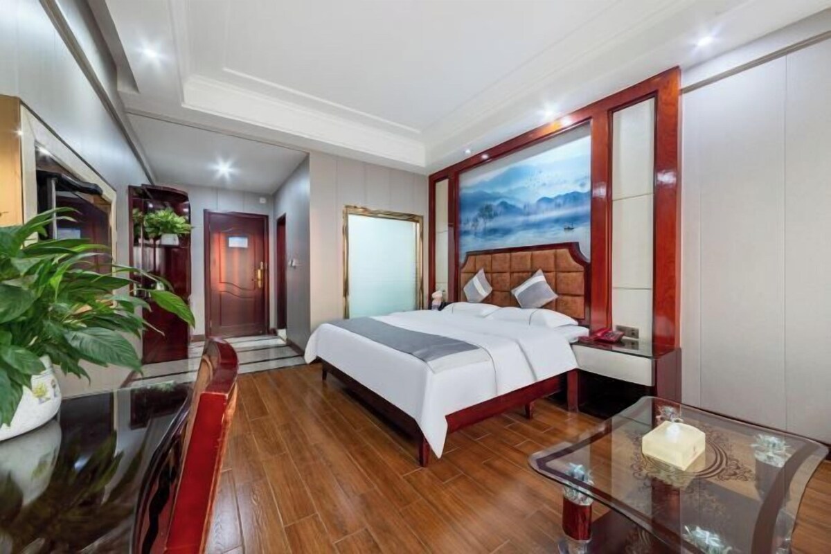 A hotel room with a bed, bedside table, and a large window with a view.