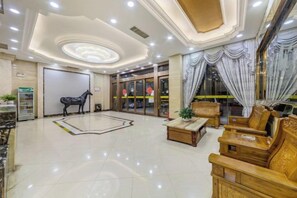 Un hall d’hôtel doté d’un sol en marbre, d’un comptoir de réception, d’un espace salon avec des meubles en bois et d’un grand miroir qui reflète l’intérieur.