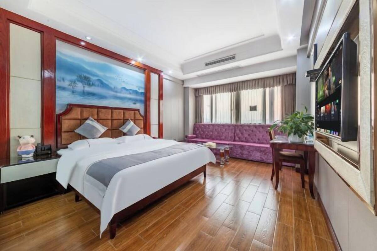 Habitación de hotel con cama, sofá, escritorio con planta y televisor.