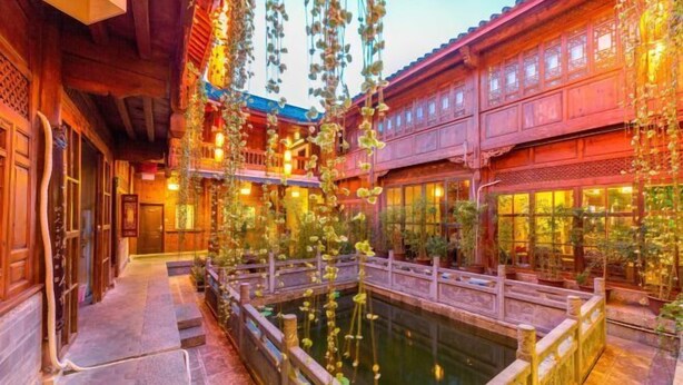 A traditional courtyard with a central pond, wooden walkways, and hanging plants. - Mu Shi Yuan Inn (Lijiang)