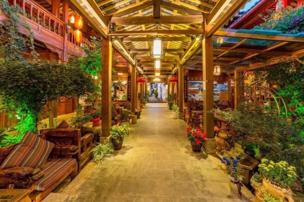 A corridor with wooden beams and a tiled floor, flanked by potted plants and furniture.