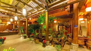 A traditional wooden interior with a high ceiling, wooden beams, and a variety of potted plants and furniture. - Mu Shi Yuan Inn (Lijiang)