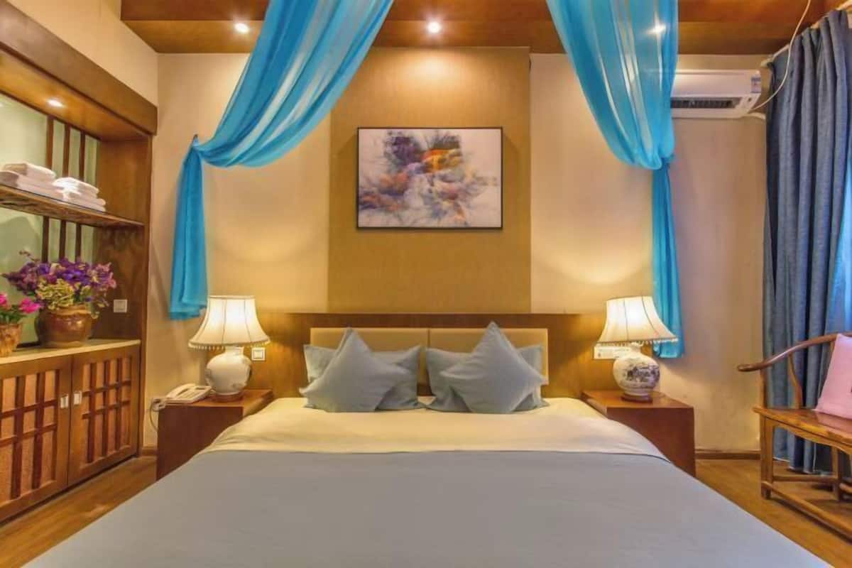 A hotel room with a bed, two bedside tables, a nightstand, a wall-mounted painting, and blue curtains.