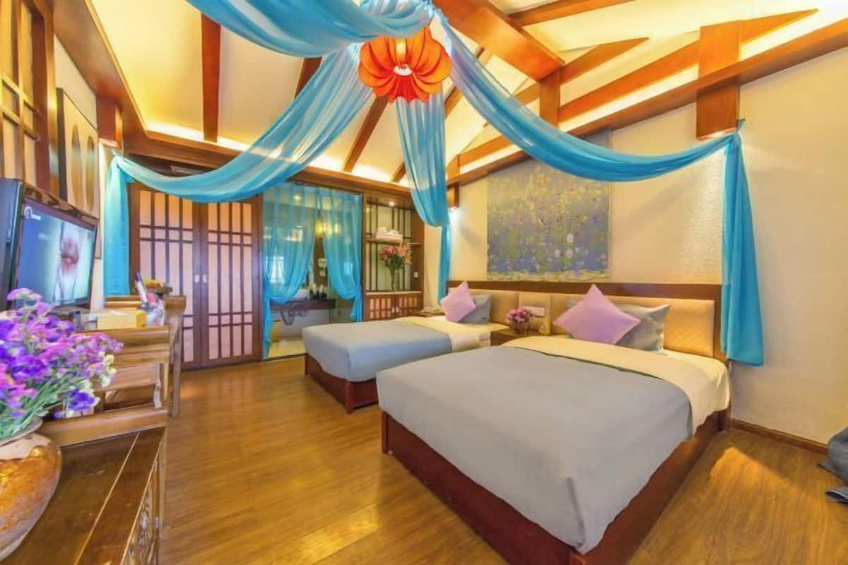 A hotel room with two beds, wooden flooring, a TV, and a decorative ceiling.