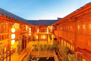 A traditional courtyard with wooden buildings, a central water feature, and a balcony.