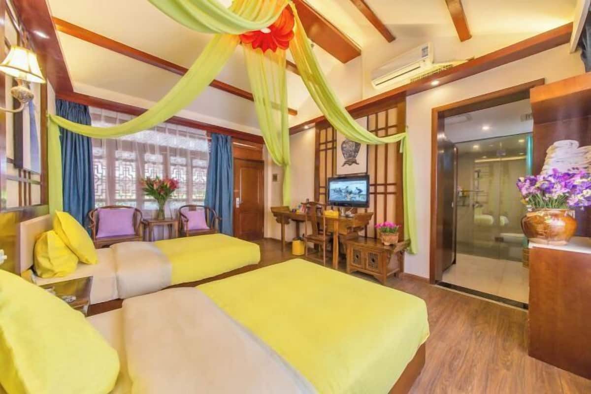 A hotel room with a bed, a desk, a television, and a bathroom visible through a glass door.
