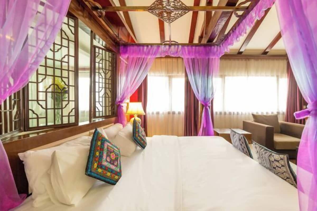 A hotel room with a bed, a sofa, a window with curtains, and a lamp.