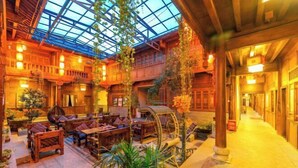 An indoor atrium with wooden architecture, a glass ceiling, and seating areas with tables and chairs. - Mu Shi Yuan Inn (Lijiang)