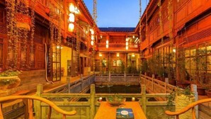 A traditional courtyard with wooden buildings, a central water feature, and a wooden table with a book. - Mu Shi Yuan Inn (Lijiang)